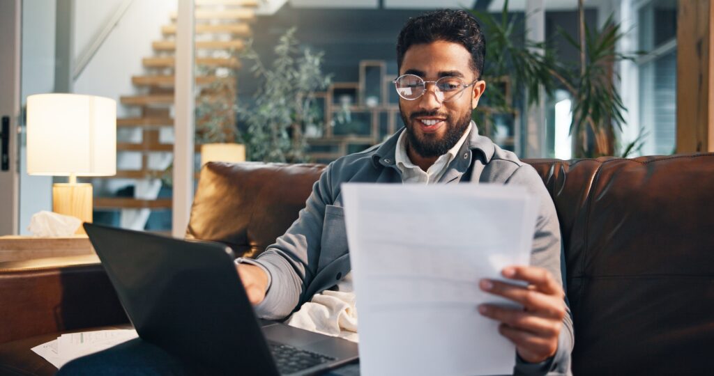 Man reading paper on couch with laptop